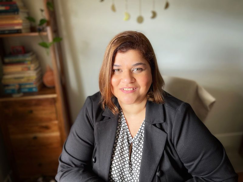 Maria de Moya of the Tombras School of Advertising and Public Relations sits in an office chair in front of a bookshelf.